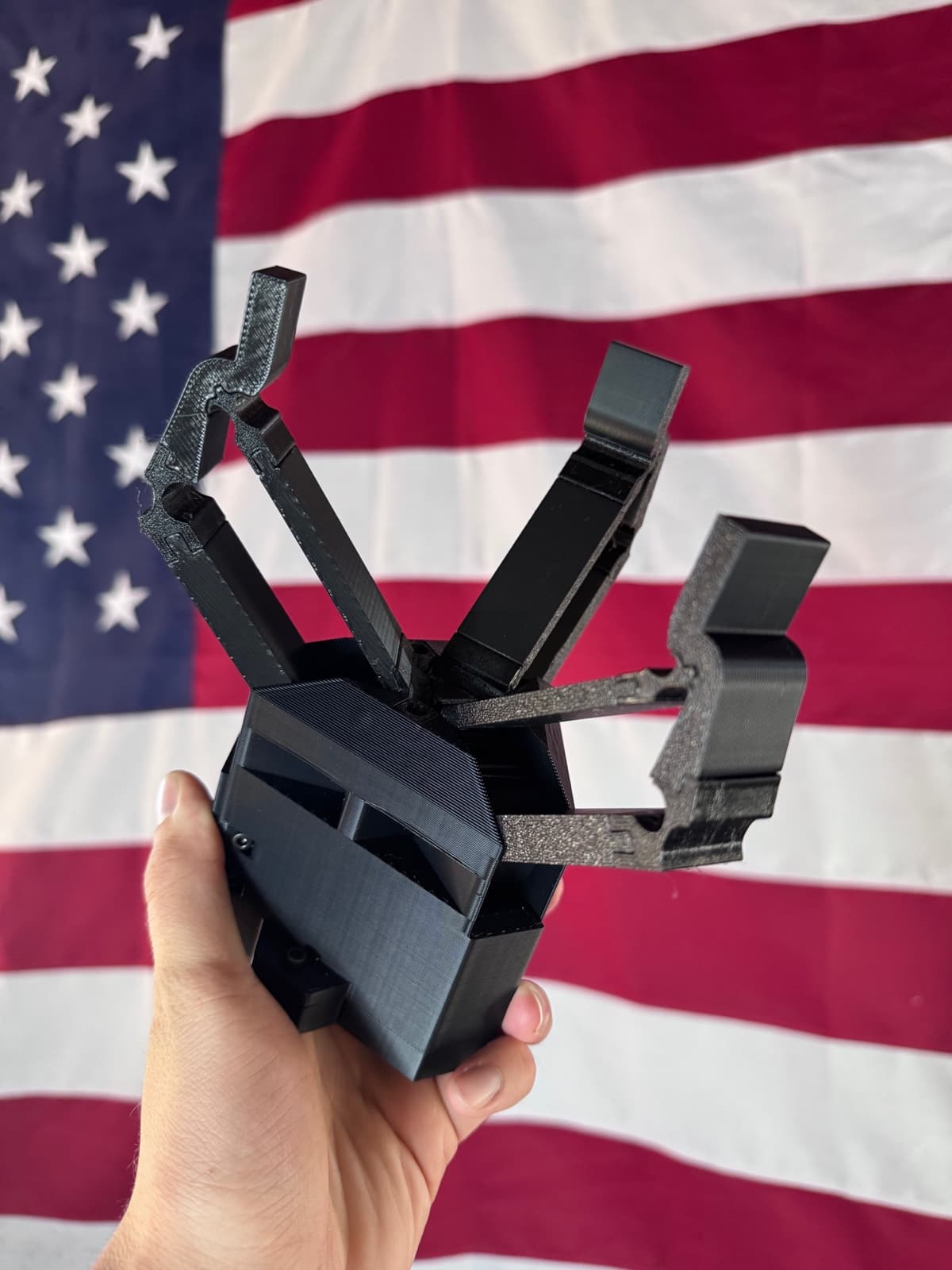 Nibbler v1.1 three-jaw gripper held in hand in front of an American flag.